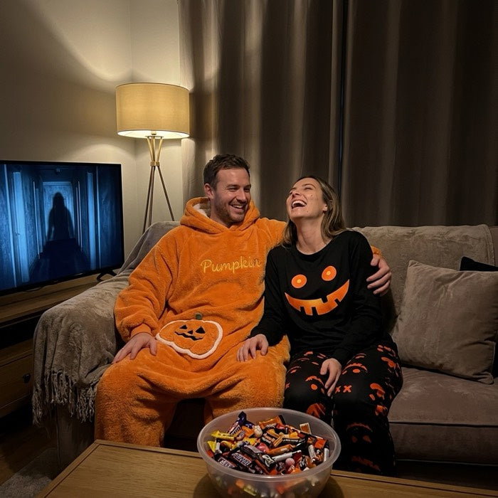 Couple on a couch, he in a pumpkin fleece onesie and she in pumpkin pyjamas