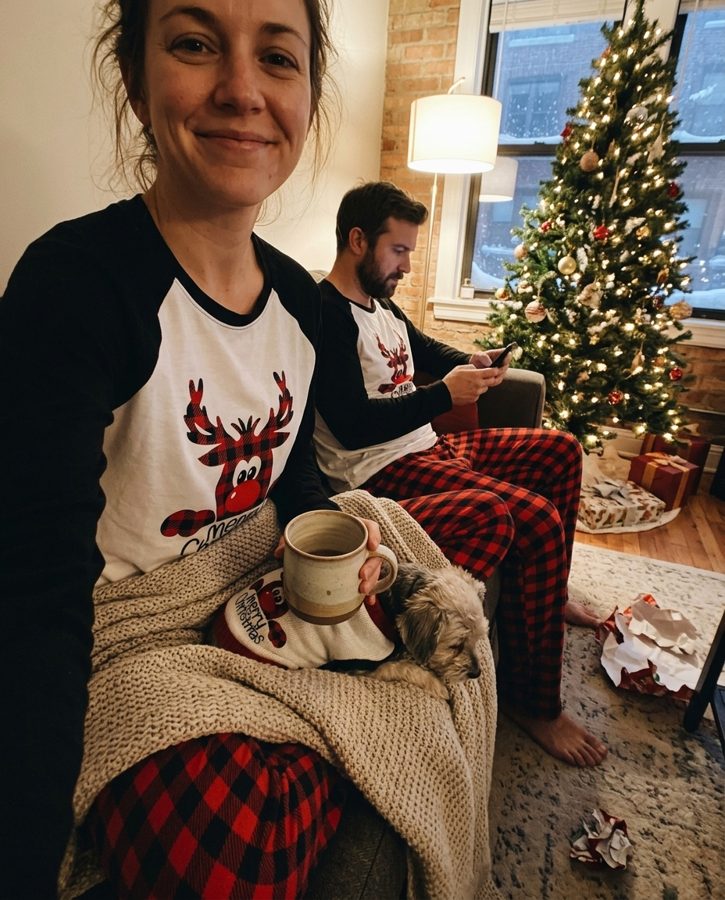 Couple in matching red plaid reindeer pajamas by the tree on Christmas morning